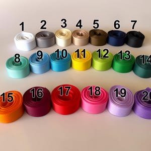 May include: A collection of twenty spools of grosgrain ribbon in various colors, including white, gray, yellow, and blue. Each spool is labeled with a number from 1 to 20.