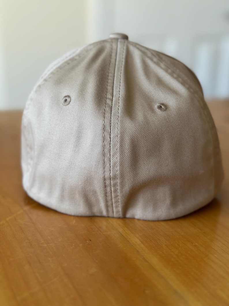 K&ouml;nnte beinhalten: Eine beige Baseballkappe mit flachem Schirm und einer Naht, die die Mitte der Krone entlangl&auml;uft.