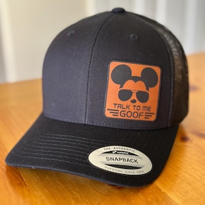 May include: Black and orange baseball cap with a brown patch featuring a cartoon Mickey Mouse wearing sunglasses and the text "Talk to me Goof". The cap has a black mesh back and a black "The Authentic Yupoong Snapback" label on the back.