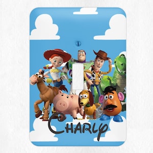 May include: A light blue light switch cover with a cartoon image of characters from the Toy Story movie franchise. The characters include Woody, Buzz Lightyear, Jessie, Bullseye, Rex, and Mr. Potato Head. The text "CHARLY" is written in a whimsical font at the bottom of the cover.
