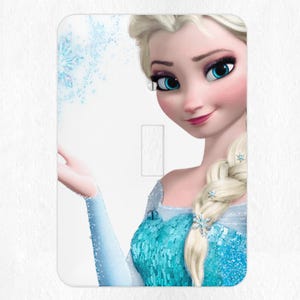May include: A light blue and white light switch cover featuring a portrait of Elsa from the movie Frozen. Elsa is wearing a blue and silver dress and has a braid in her hair. She is holding her hand out with snowflakes around her.