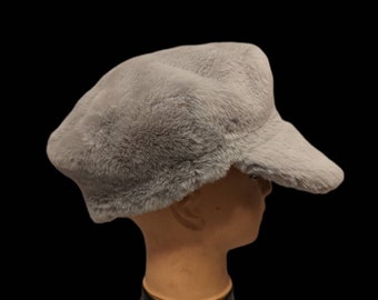 May include: A light gray faux fur newsboy cap with a curved brim. The cap is on a mannequin head.