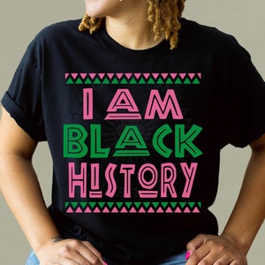 Puede incluir: Camiseta negra con el texto "I AM BLACK HISTORY" en letras rosas y verdes con un patrón geométrico.