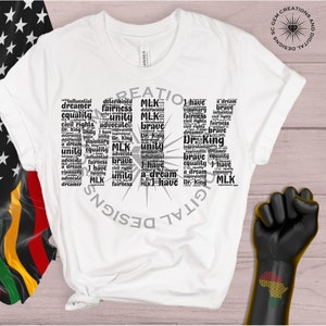 May include: A white t-shirt with a black word cloud design featuring the words "I have a dream", "MLK", "unity", "equality", "fairness", "brave", "civil rights", "inspirational", "dreamer", and "advocate".