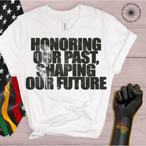 May include: White t-shirt with black text that reads "HONORING OUR PAST, SHAPING OUR FUTURE". A black and white photo of a man is incorporated into the text.