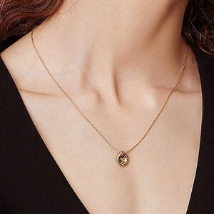May include: A gold chain necklace with a small, round pendant. The pendant has a textured, abstract design.