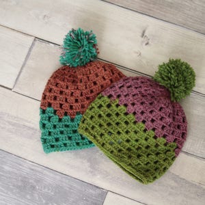 Puede incluir: Dos gorros de punto con pompones. Un gorro es verde, marrón y rojo. El otro gorro es verde, marrón y morado.