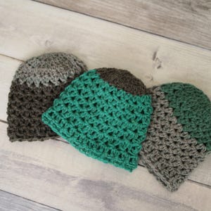 Puede incluir: Tres gorros de ganchillo en colores marrón y verde azulado. Los gorros están hechos con un patrón de punto texturizado.