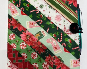 May include: A quilted Christmas-themed journal cover with a pen attached. The cover features diagonal stripes of fabric in red, green, and white, adorned with poinsettias, candy canes, and holiday motifs. A black button and a teal pen are attached.