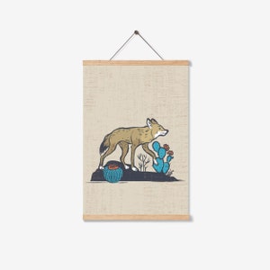 May include: A framed print featuring a coyote walking past cacti. The coyote is tan and brown, the cacti are blue and green, and the background is a light beige. The print is held by wooden magnetic poster hangers.