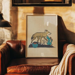 May include: A framed art print featuring a tan coyote walking across a dark rock formation. The scene includes a round blue cactus with orange flowers and a taller blue prickly pear cactus with red blossoms against a light beige background.