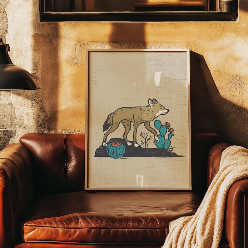 May include: A framed art print featuring a tan coyote walking across a dark rock formation. The scene includes a round blue cactus with orange flowers and a taller blue prickly pear cactus with red blossoms against a light beige background.