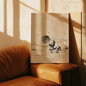Puede incluir: Una impresi&oacute;n art&iacute;stica enmarcada que presenta a un vaquero montado a caballo bajo una gran luna. La ilustraci&oacute;n en blanco y negro representa un paisaje des&eacute;rtico con monta&ntilde;as y estrellas. La obra de arte tiene una est&eacute;tica vintage y r&uacute;stica.