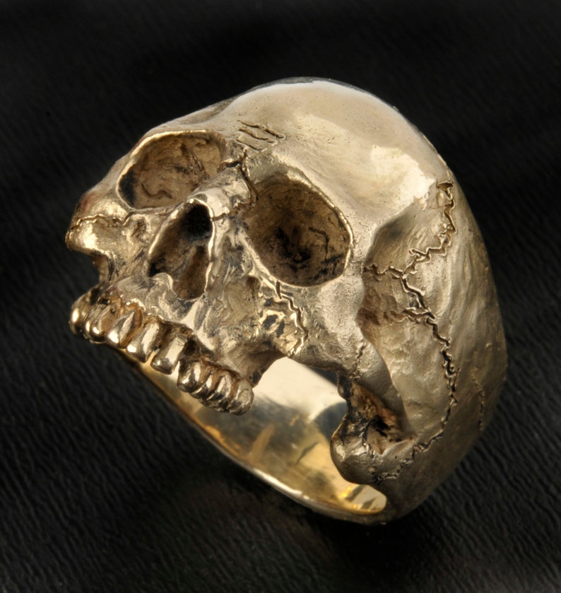 May include: A gold skull ring with detailed features, including teeth and a textured surface.