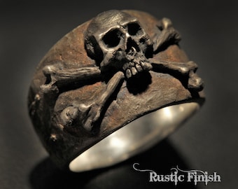May include: A silver skull and crossbones ring with a rustic finish. The ring is made of metal and has a detailed design.