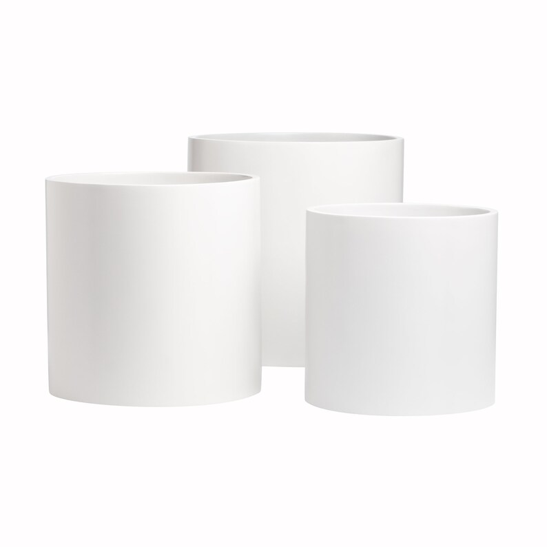 May include: Three white cylindrical ceramic planters of varying sizes. The planters are arranged in a staggered formation, with the largest planter in the back and the smallest planter in the front.