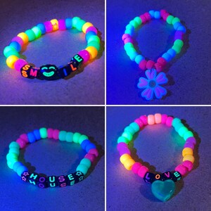 May include: Four colorful beaded bracelets. One bracelet spells "SMILE" with a smiley face bead. Another has a flower pendant. The third spells "HOUSE". The last bracelet spells "LOVE" with a heart pendant. All glow under a black light.