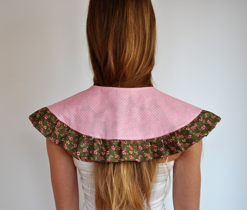 May include: A pink and green fabric collar with a ruffled edge. The collar is made of a polka dot fabric with a floral print on the ruffle.