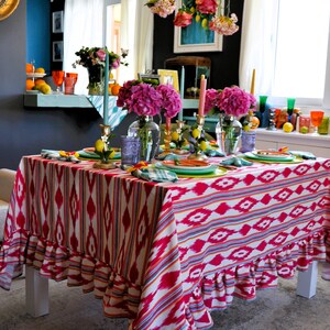 Peut inclure: Une nappe rose et blanche avec un motif g&eacute;om&eacute;trique et des bords festonn&eacute;s. La nappe est dress&eacute;e pour un d&icirc;ner avec des fleurs roses, des citrons et des bougies.