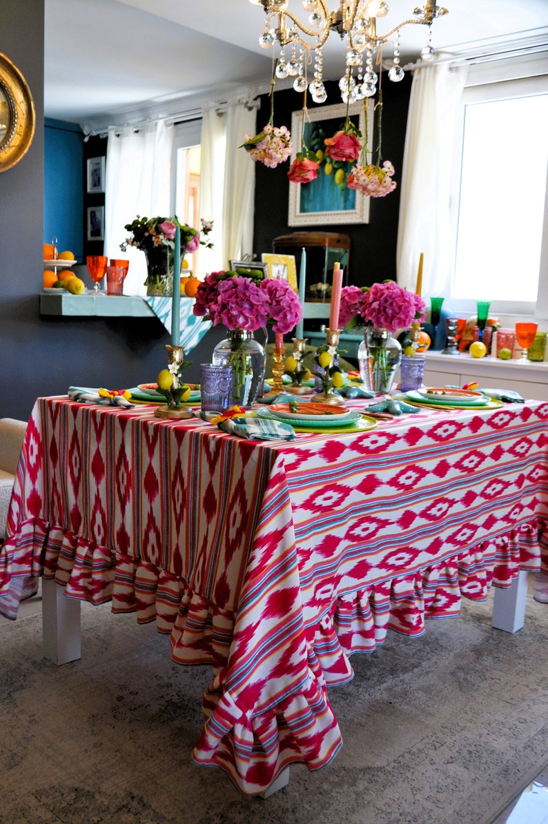 Peut inclure: Une nappe rose et blanche avec un motif g&eacute;om&eacute;trique et des bords festonn&eacute;s. La nappe est dress&eacute;e pour un d&icirc;ner avec des fleurs roses, des citrons et des bougies.