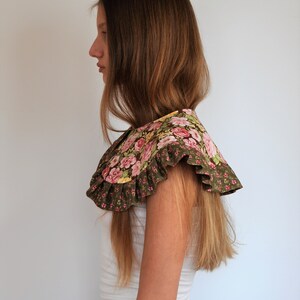 May include: A woman wearing a white shirt and blue jeans with a floral print collar. The collar is brown with pink and yellow flowers.