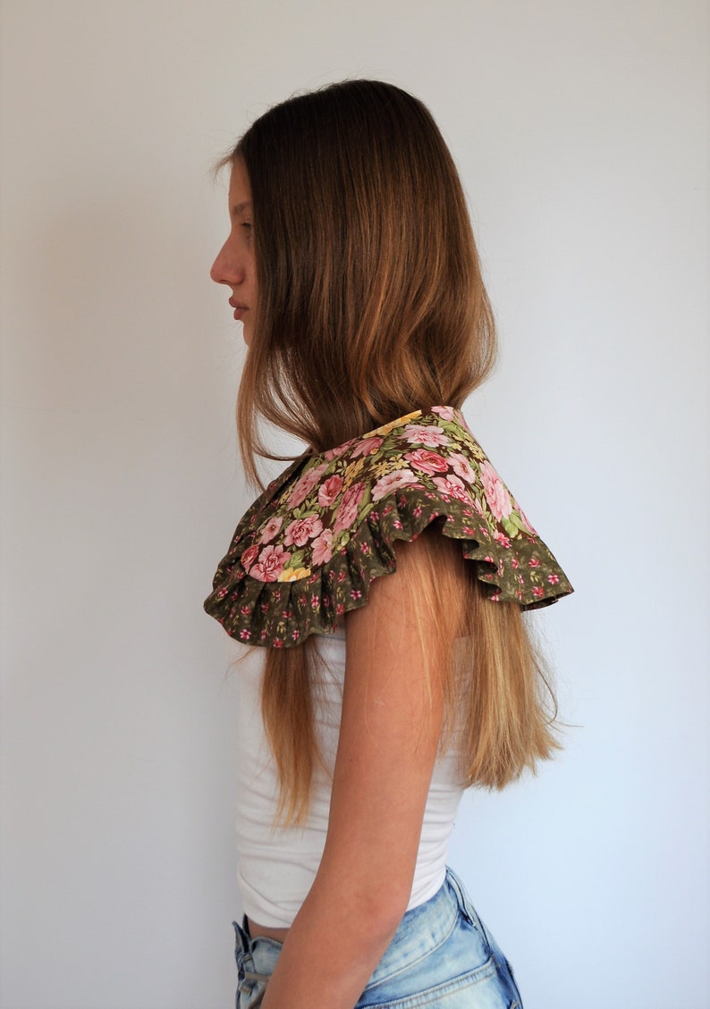 May include: A woman wearing a white shirt and blue jeans with a floral print collar. The collar is brown with pink and yellow flowers.