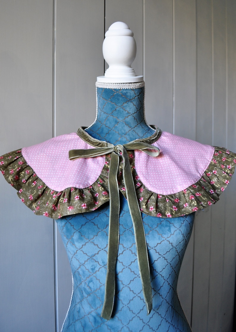 May include: A pink and green fabric collar with a velvet bow. The collar has a ruffled edge and a polka dot pattern.