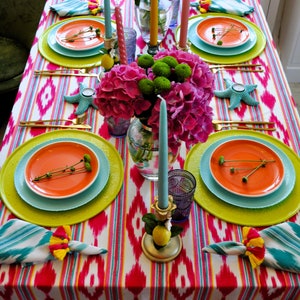 Peut inclure: Une composition florale rose et verte avec des bougies sur une table dress&eacute;e avec une nappe ray&eacute;e color&eacute;e et des assiettes.