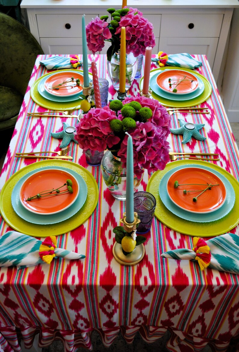 Peut inclure: Une composition florale rose et verte avec des bougies sur une table dress&eacute;e avec une nappe ray&eacute;e color&eacute;e et des assiettes.