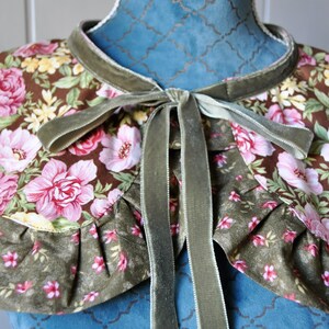May include: A green velvet ribbon tied into a bow around a floral fabric collar. The collar has a brown background with pink and yellow flowers.