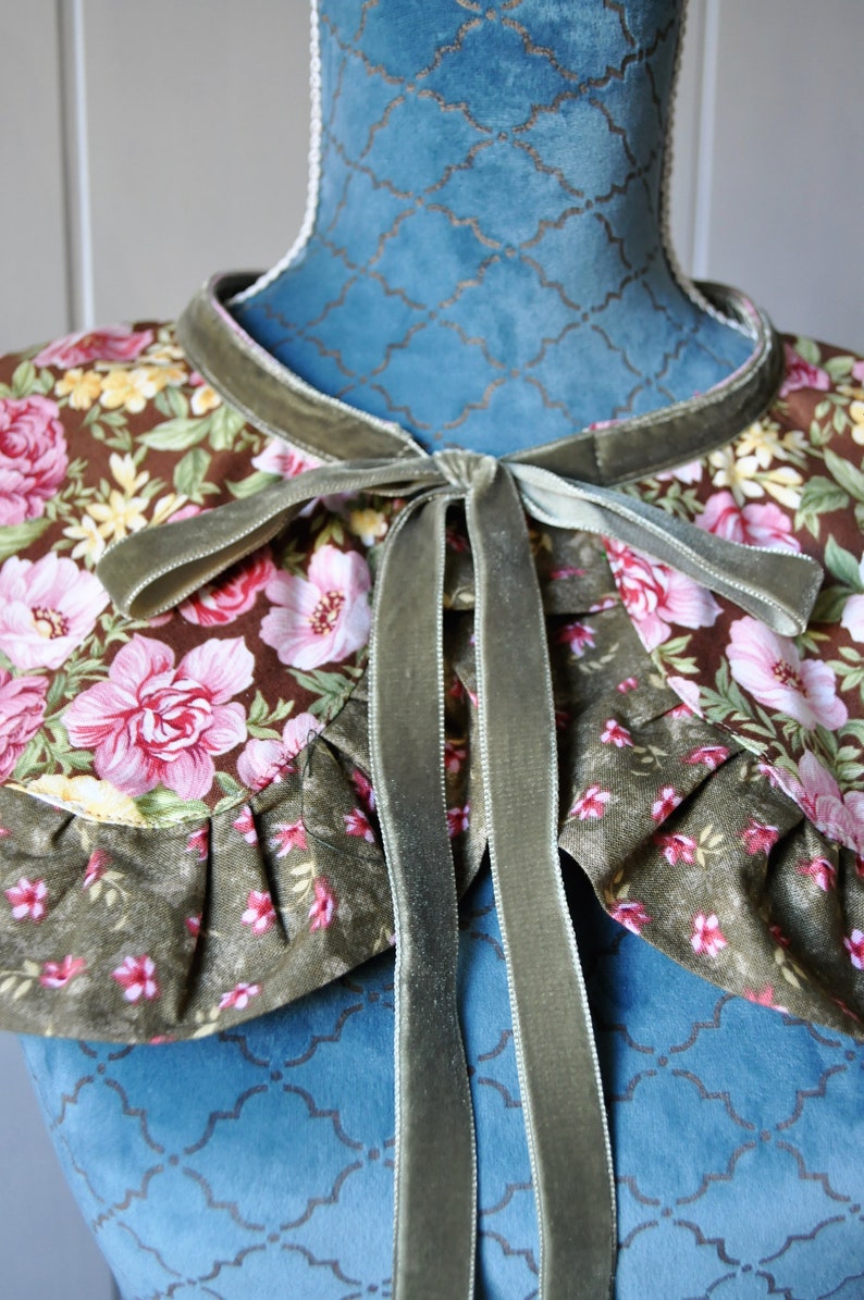 May include: A green velvet ribbon tied into a bow around a floral fabric collar. The collar has a brown background with pink and yellow flowers.
