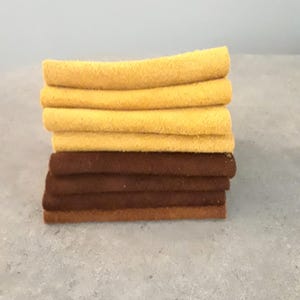 May include: A stack of seven rectangular felt fabric pieces arranged horizontally. The top four pieces are a vibrant mustard yellow, while the bottom three pieces are a deep, solid chocolate brown. Each piece has a soft, textured surface.