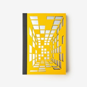 Op de afbeelding: Een geel notitieboek met een zilveren, geometrisch, 3D-ontwerp dat uit de kaft is geknipt.