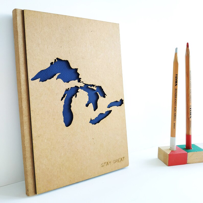 May include: A brown notebook with a blue cutout of the Great Lakes and the text "STAY GREAT" on the front.