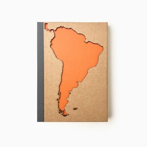 May include: A brown notebook with a cutout of the continent of South America in orange. The notebook has a grey spine.