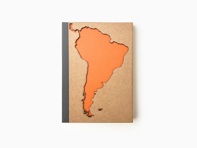 May include: A brown notebook with a cutout of the continent of South America in orange. The notebook has a grey spine.
