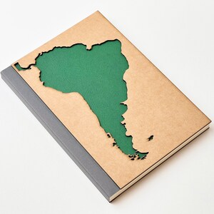 May include: A brown notebook with a cut-out shape of South America. The cut-out is filled with green fabric.