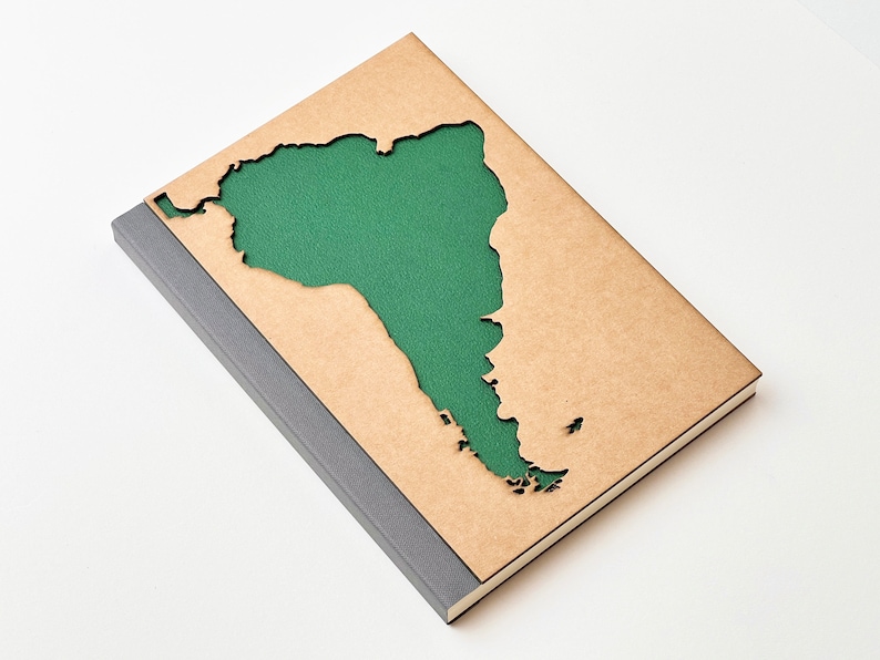 May include: A brown notebook with a cut-out shape of South America. The cut-out is filled with green fabric.
