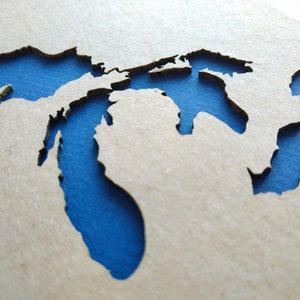 May include: A wooden cutout of the Great Lakes, painted blue. The cutout is on a light brown background.