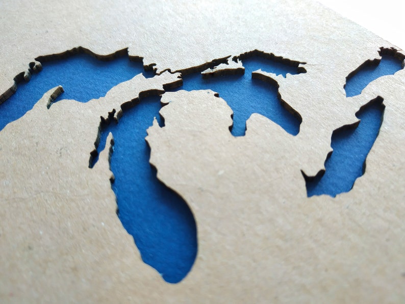 May include: A wooden cutout of the Great Lakes, painted blue. The cutout is on a light brown background.