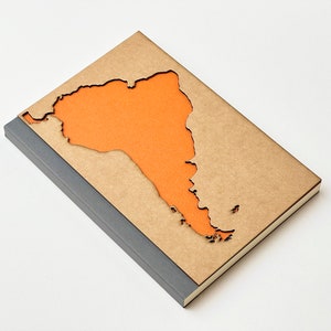 May include: A brown notebook with a cut-out shape of South America. The cut-out is filled with orange paper. The notebook has a grey spine.