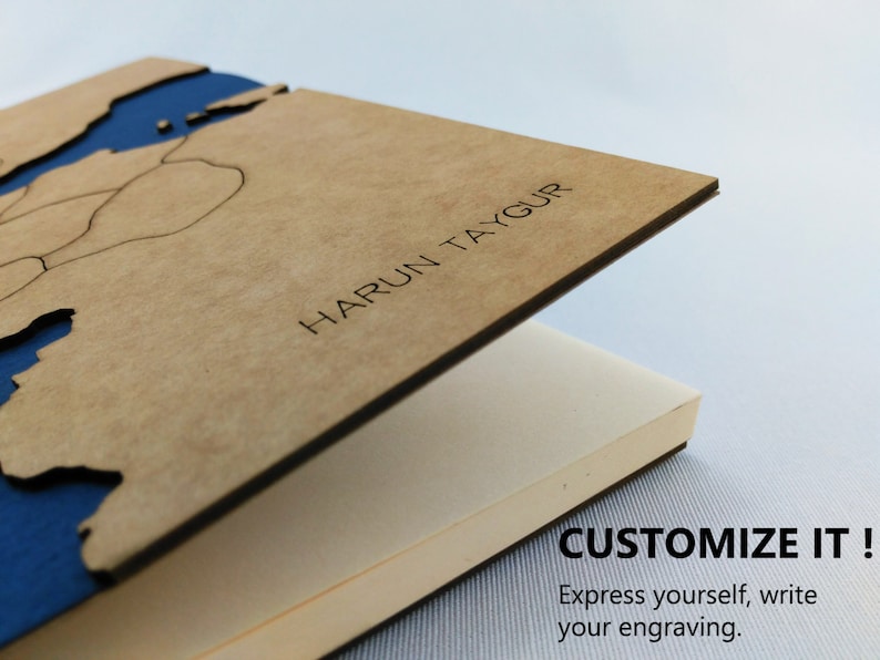 May include: A brown wooden notebook with a blue map design on the cover. The cover is open to reveal blank pages. The notebook is personalized with the name "HARUN TAYGUR".