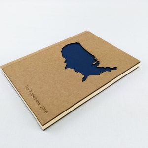 Puede incluir: Una libreta marr&oacute;n con una forma recortada de los Estados Unidos de Am&eacute;rica. El recorte est&aacute; relleno con un papel azul oscuro. La libreta tiene el texto "The Paperbons 2016" impreso en la portada.