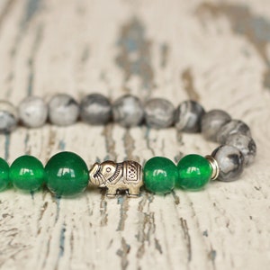 Puede incluir: Un brazalete con cuentas grises y verdes y un dije de elefante plateado.