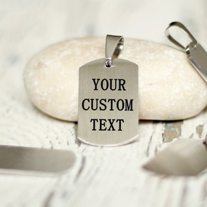 Puede incluir: Cuatro chapas de perro de metal plateado, una con el texto "YOUR CUSTOM TEXT" grabado en ella.