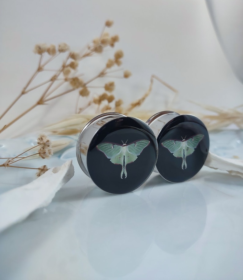 May include: Pair of black and silver ear gauges with a green luna moth design.
