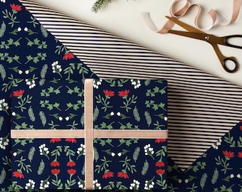 May include: A wrapped gift with a navy blue floral patterned wrapping paper, tied with a tan ribbon. The floral pattern includes red flowers, white berries, and green leaves. A striped wrapping paper and scissors are also visible.