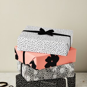 May include: A stack of four gift boxes wrapped in black and white patterned paper. The top box has a black ribbon tied in a bow. The boxes are sitting on a white surface.