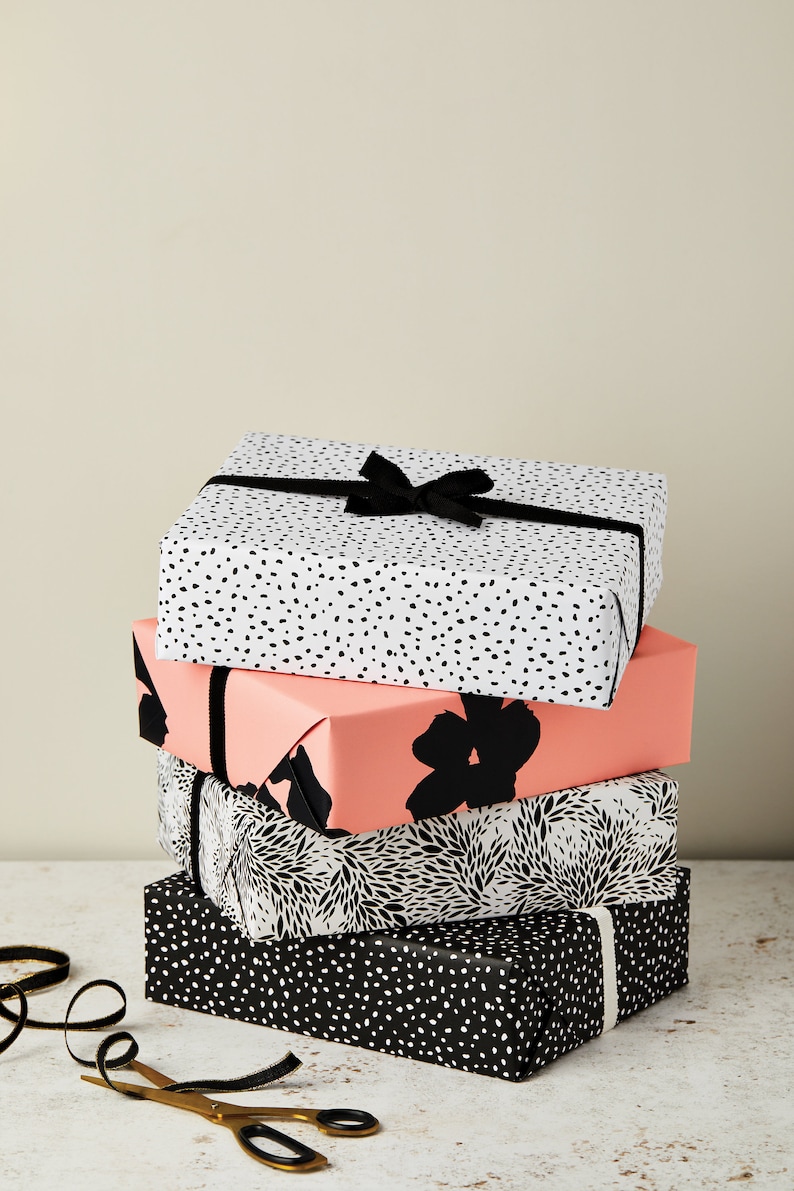 May include: A stack of four gift boxes wrapped in black and white patterned paper. The top box has a black ribbon tied in a bow. The boxes are sitting on a white surface.