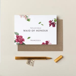 May include: A white card with pink and burgundy flowers printed on it. The card says "Thank you for being my Maid of Honour" and is signed "Francesca".